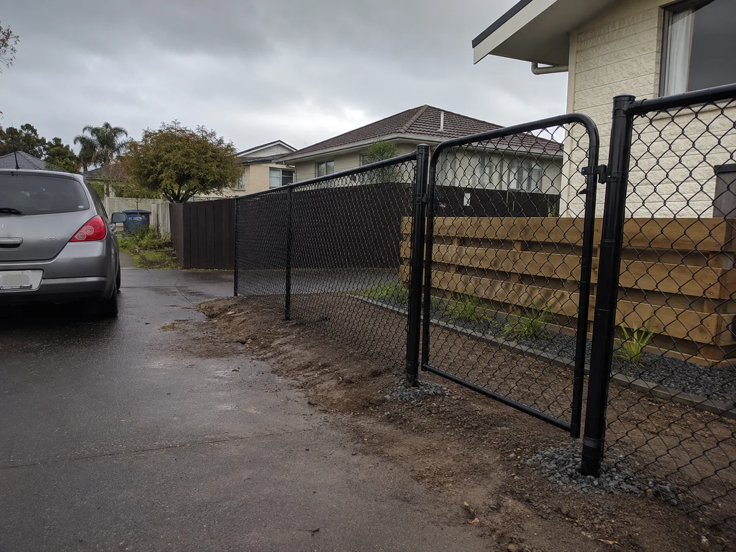 Black chain-link driveway gate across a wet residential driveway