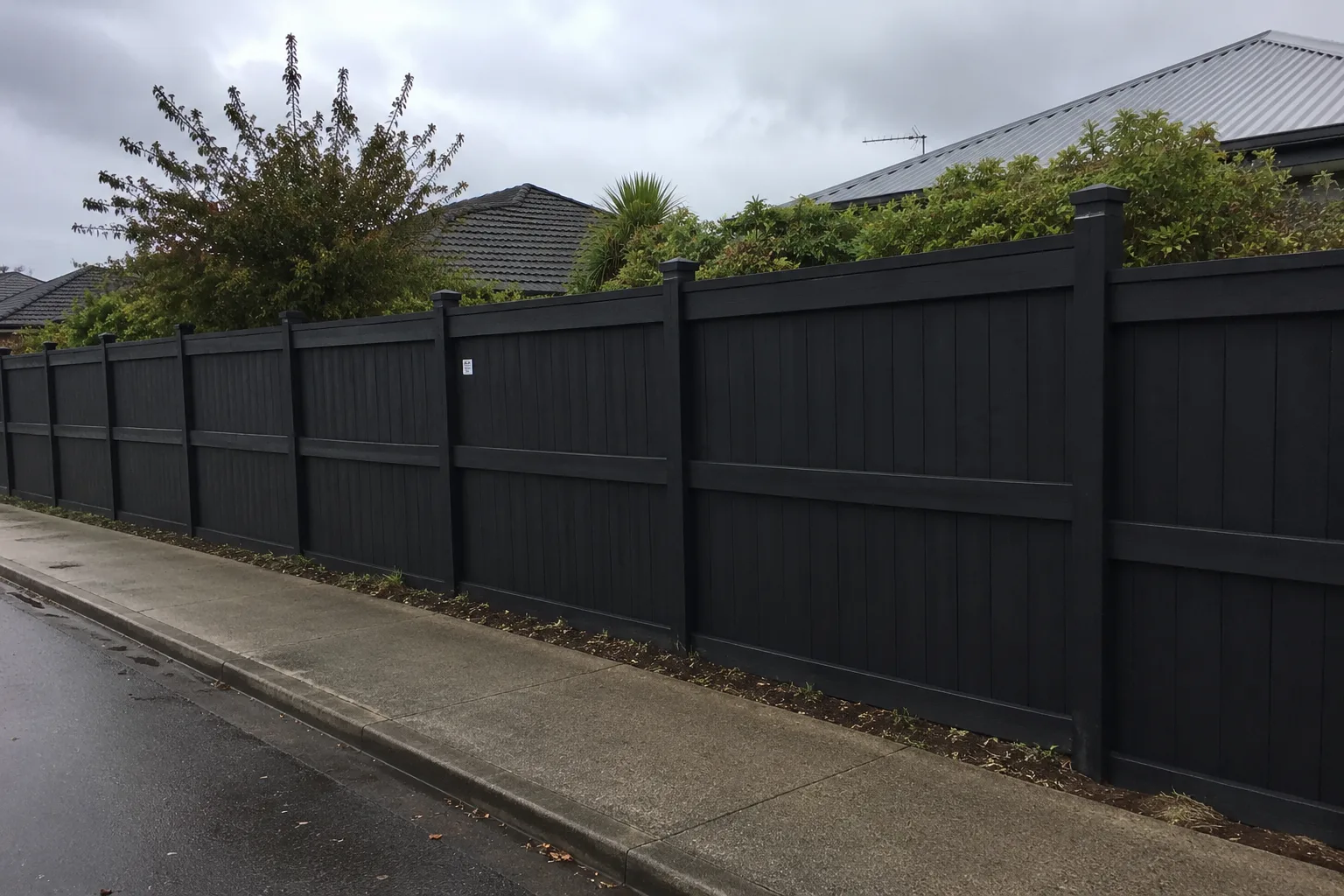 Black painted timber boundary fence running beside a residential street