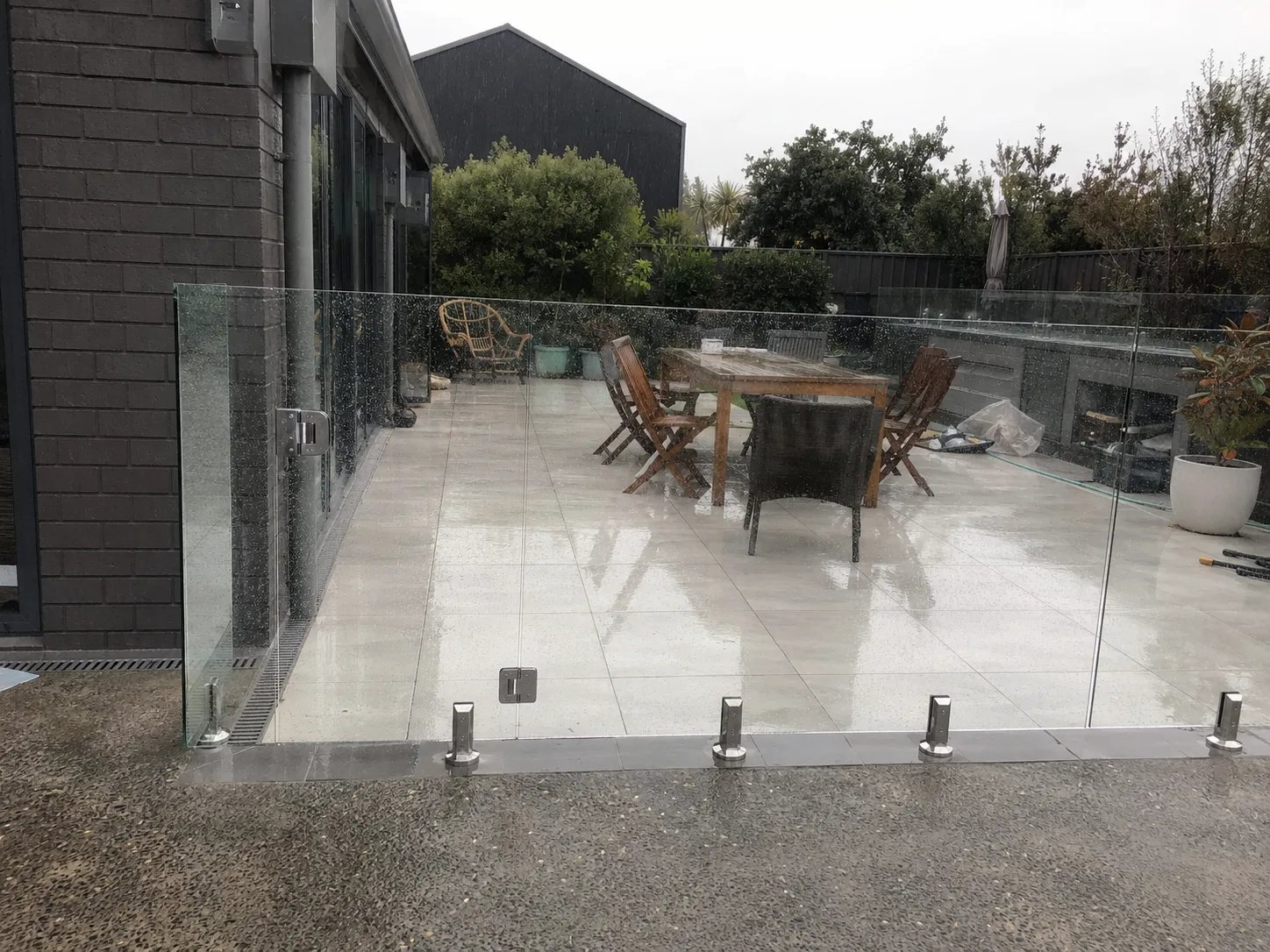 Frameless glass barrier around a rain-wet residential patio