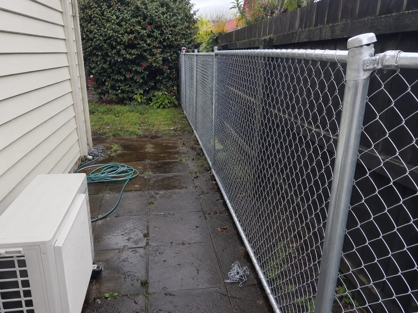 Galvanised chain-link fence beside a narrow wet residential path