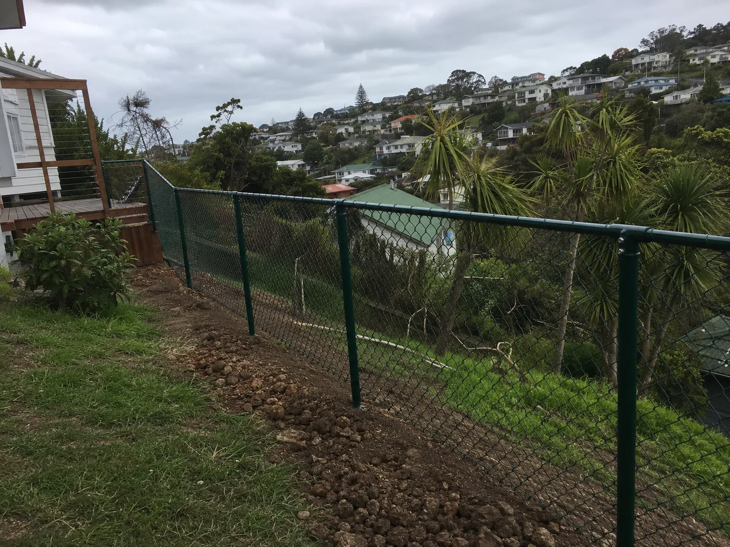Green chain-link boundary fence descending a steep hillside
