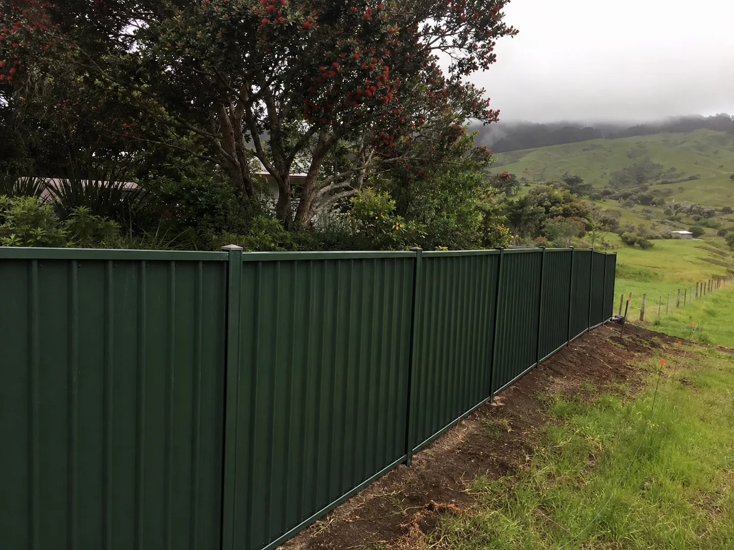 Dark green steel panel fence following a rural slope