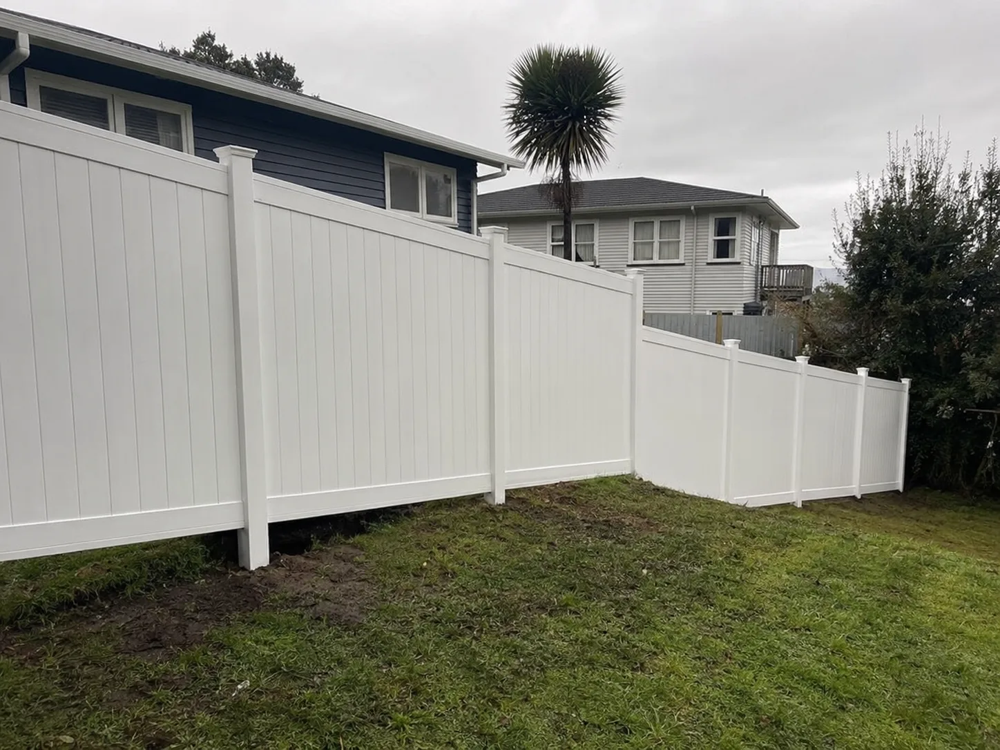 Stepped white PVC privacy fence following a sloping boundary