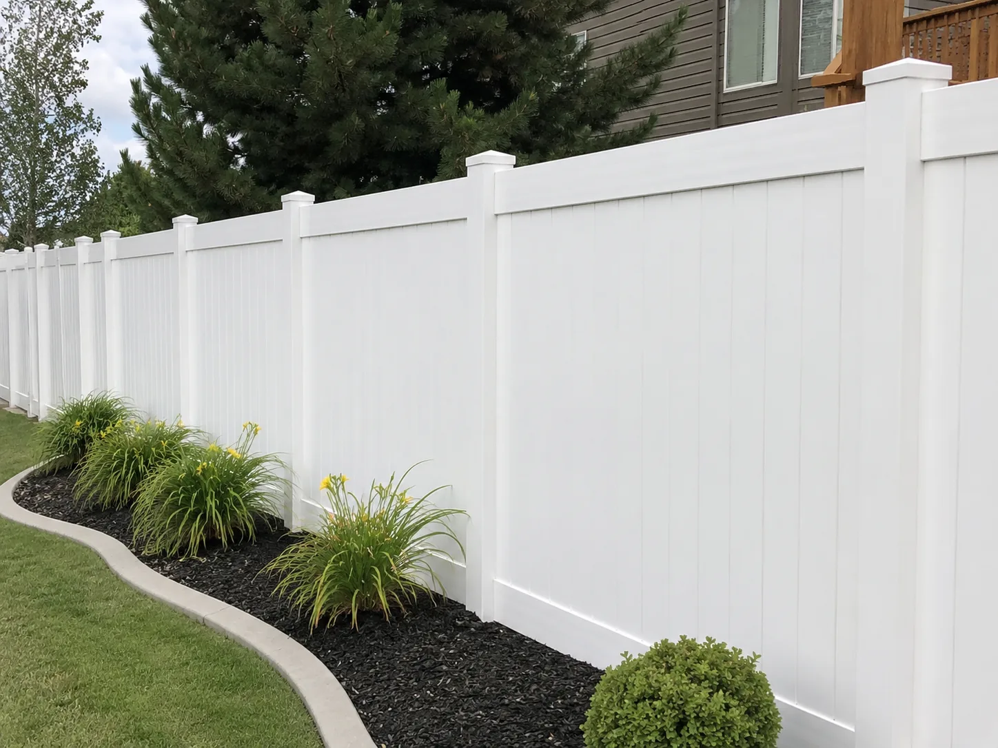 White PVC privacy fence bordering a landscaped lawn and garden