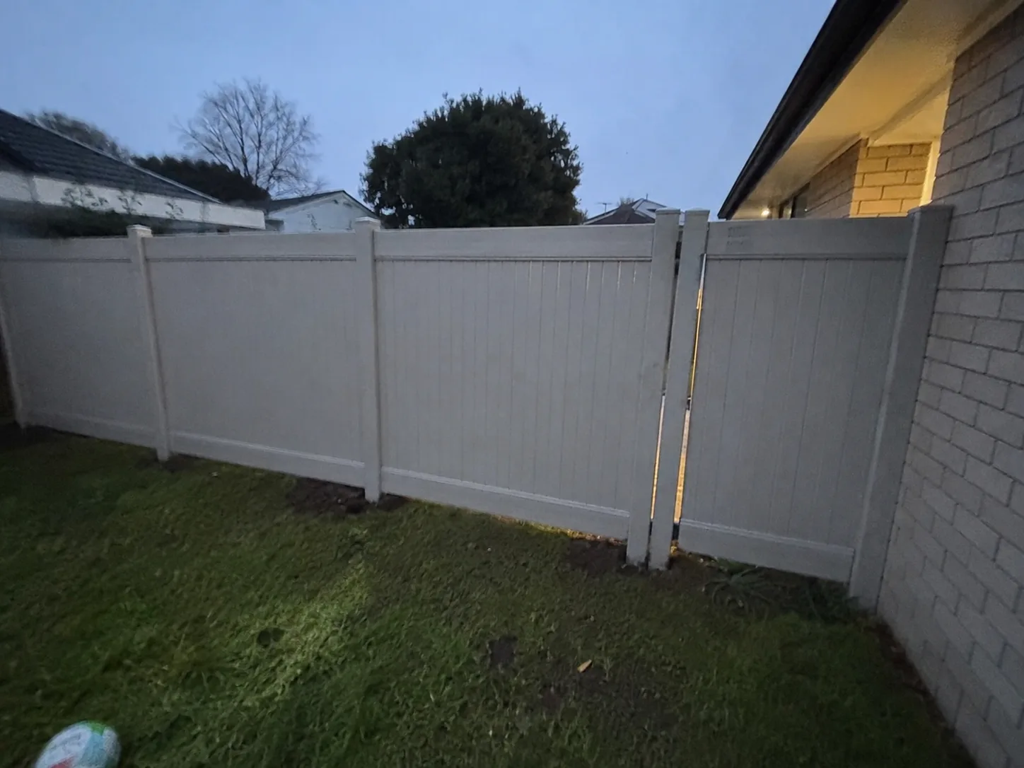 White PVC privacy fence enclosing a residential yard at dusk